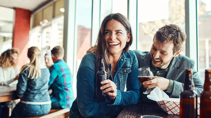 Alcohol is always good for those first date nerves. a young couple having drinks in a bar with people blurred in the background.