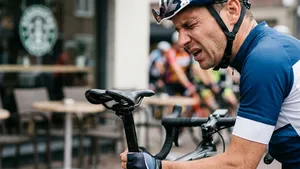 Wielrenner stapt met een pijnlijk vertrokken gezicht weer op zijn racefiets, als illustratie van zadelpijn na een pauze.