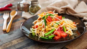 Traditional Thai food papaya salad prepared with fine slices of papaya, tomatoes, green beans and peanuts.