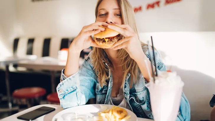 Young woman eating burger in restaurant