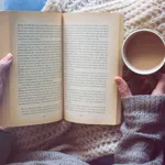 a woman is reading a book and holding coffee