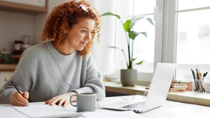 Cute university student with curly red hair doing homework sitti