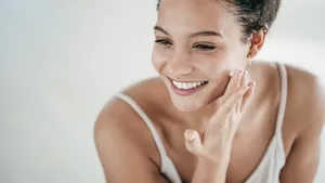 Smiling young women applying moisturiser to her face