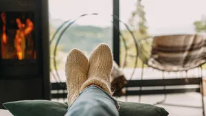 Close-up van voeten in dikke wollen sokken onder een warm dekentje en houtkachel, hét redmiddel voor vrouwen die altijd koude voeten hebben