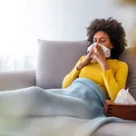 Woman blowing her nose on couch at home in the living room.