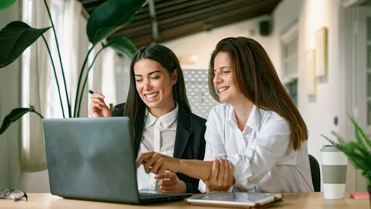 Cheerful female colleagues using laptop together