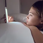 Teenage girl with mobile phone lying in bed at night