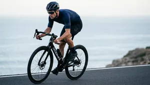 Een professioneel ogende wielrenner in een strakke, gesponsorde outfit rijdt op een glimmende, dure carbon racefiets. De foto heeft een schone, commerciële uitstraling, alsof het een reclame is.