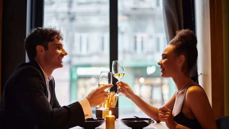 cheerful african american woman clinking glasses of wine with man during date on Valentines day