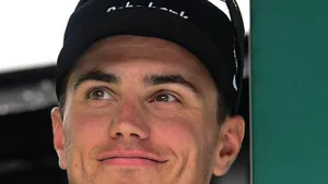 Portret van Olav Kooij met glimlach tijdens een wielerwedstrijd, close-up met neutrale achtergrond.