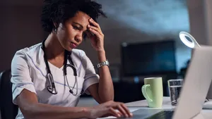 African American female doctor with headache working on laptop.