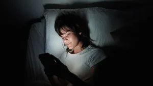 Young woman using her cellphone while lying in bed at night