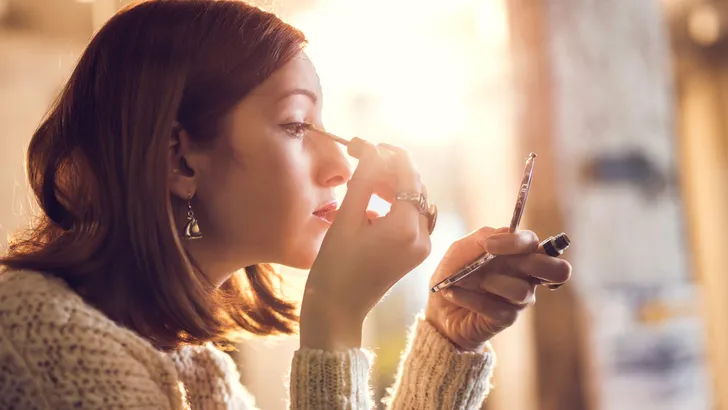 Woman holding hand mirror and fixing make-up.