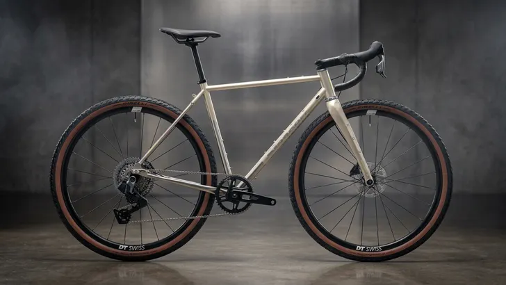 "Een studio-opname van een champagnekleurige Standert Erdgeschoss-gravelbike, in zijprofiel tegen een egale lichtgrijze achtergrond. De fiets heeft een stalen frame