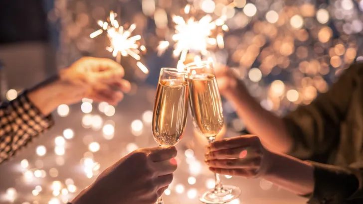 Hands of couple with flutes of champagne and their friends with bengal lights