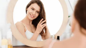 Smiling blonde girl looking at mirror, touching her hair