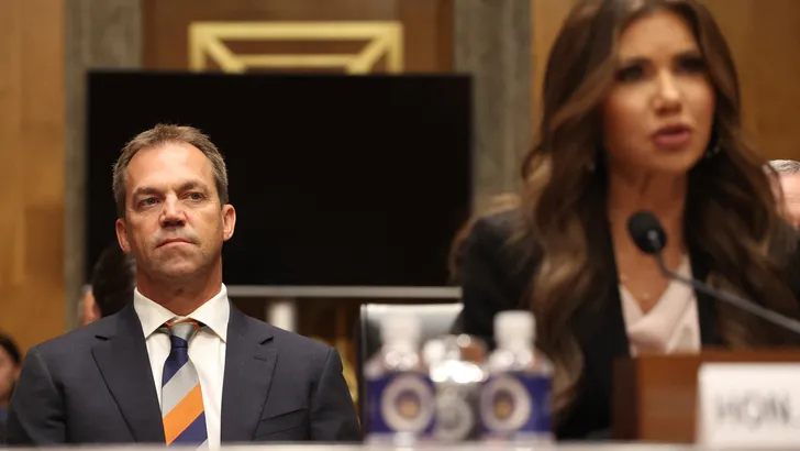 Bryon Noem op de achtergrond, met zijn vrouw Kristi Noem als spreker.