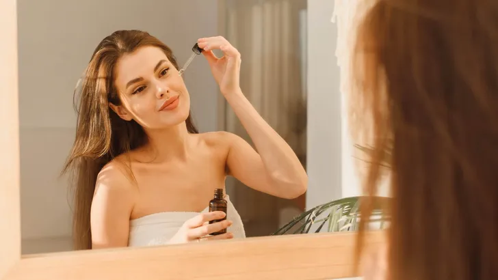 A beautiful young woman uses a moisturizing anti-aging facial serum in the bathroom. Body skin care and cosmetic application concept