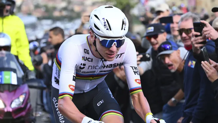 adej Pogačar in de regenboogtrui tijdens een zware klim, zichtbaar in volle inspanning tussen juichende fans, symbool voor de extreme wattages van het moderne wielrennen.