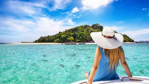 A beautiful tourist woman with sunhat sits on a yacht and looks at the turquoise sea and beaches of Bamboo island in the Krabi region, Thailand