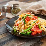 Traditional Thai food papaya salad prepared with fine slices of papaya, tomatoes, green beans and peanuts.