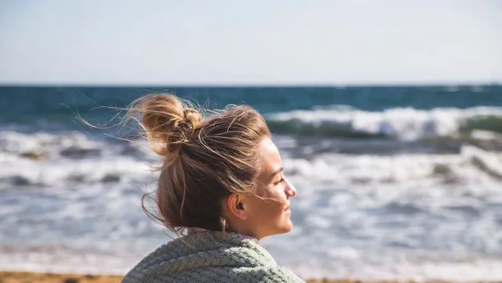 Een vrouw bij de zee met een messy bun.