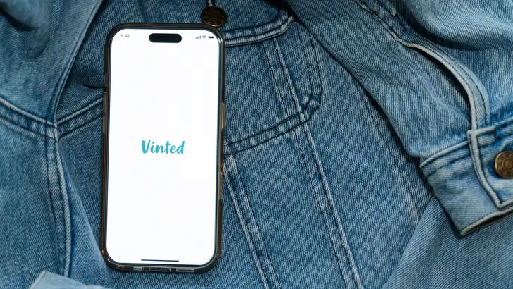 Foto van telefoon met Vinted logo op denim stof.