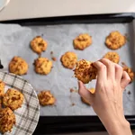 Woman collecting fresh homemade coconut cookies on a plate in the kitchen