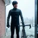 Mannelijke wielrenner in winterkleding met helm, klaar om te vertrekken op zijn geplande rustdag, kijkt zelfverzekerd naar buiten vanuit zijn deuropening.