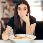 Woman Feeling Sick While Eating Bad Food in a Restaurant