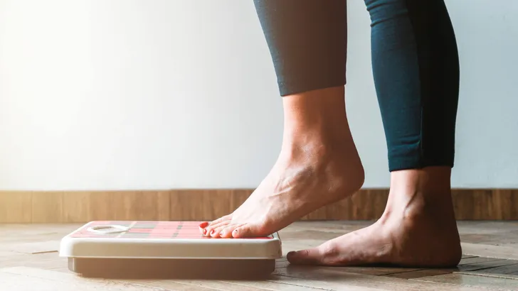 Female checking kilogrammes getting on the scale - self care and body positivity concept - warm flare on left