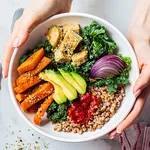 Woman hands eating vegan salad of baked vegetables, avocado, tofu and buckwheat buddha bowl, top view. Plant based food concept.