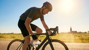 Mannelijke wielrenner met helm op fietst in de brandende zon op een Nederlandse dijk en pakt een bidon.