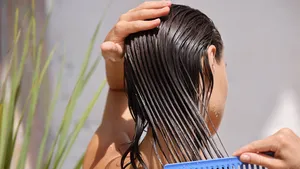 Vrouw verdeelt conditioner door handdoekdroog haar met een grove kam voor een gelijkmatige verzorging.