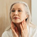 Senior woman stretching skin on her face in front of a mirror