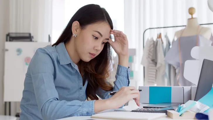 Young attractive asia female business owner thoughtful serious doubtful feel stress worry with financial problem in SME crisis small business challenges impact from covid coronavirus at home office.