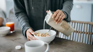 Cropped shot of young Asian mother preparing healthy breakfast, pouring milk over cereals on the kitchen counter. Healthy eating lifestyle
