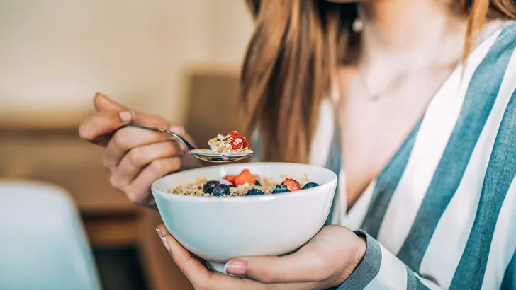 Crop woman close up eating oat and fruits bowl for breakfast