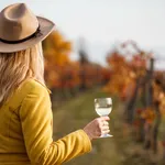 Woman vintner enjoying white wine in her vineyard at autumn