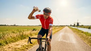 Mannelijke wielrenner met helm giet tijdens een snikhete zomerrit over een polderweg water over zijn nek voor verkoeling.