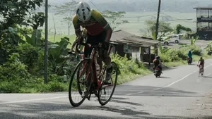 Dynamische actiefoto van een wielrenner die krachtig en in balans staand op de pedalen een berg beklimt, waarbij de fiets kantelt onder de rijder.