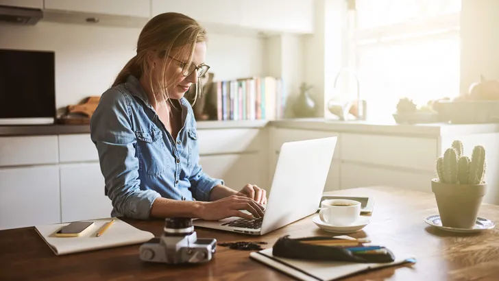 Young woman sitting in her kitchen working on a laptop