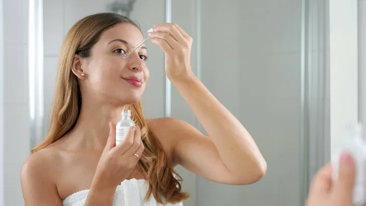 Beauty woman applying hyaluronic acid on the face in the bathroom. Skin care routine.
