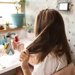 Young woman using hair spray in bedroom early in the morning