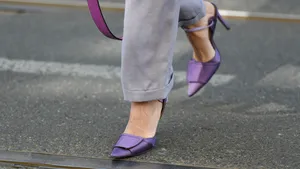 Pijnloos op hakken lopen.  – Close-up treetstyle-foto van benen met paarse naaldhakken en lichtgrijze pantalon.
