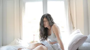 Vrouw met buikpijn zittend op bed - Acute Hepatische Porfyrie (AHP)