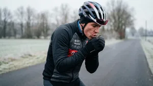 Mannelijke wielrenner met helm op blaast in zijn winterhandschoenen om koude handen op te warmen tijdens een fietsrit in de winter.
