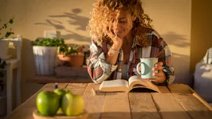 Ontspannen vrouw leest een boek met een warme kop thee aan tafel, genietend van biologische winterrust.
