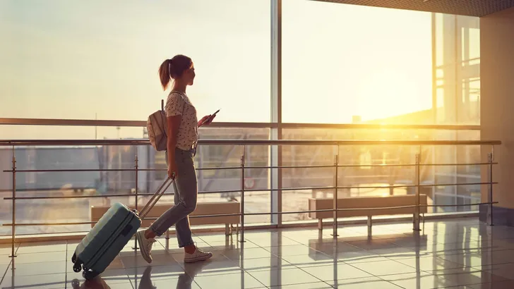 young woman goes  at airport at window with suitcase waiting for plane