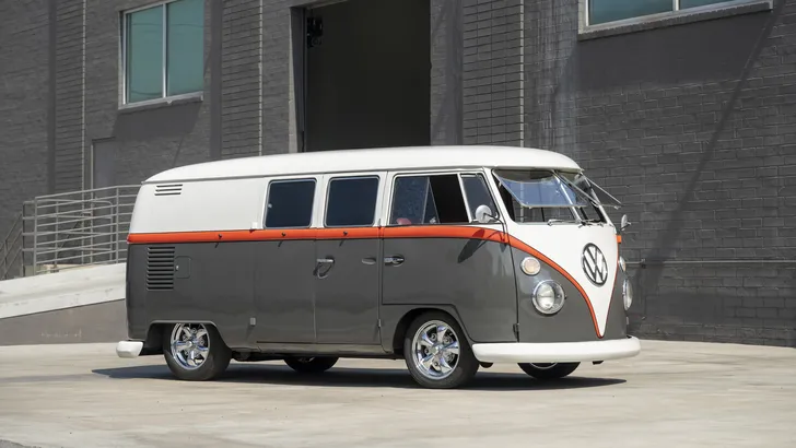 Verlaagde Volkswagen-spijlbus uit 1963 in wit, oranje en grijs, schuin van voren met geopende voorruitjes.